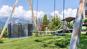 A swing set with a netted enclosure, a picnic table, and a view of mountains. - Apartment 'Patztauhof Tartscher Bühel' with Mountain View, Private Terrace and Wi-Fi (Sluderno BZ)