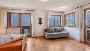 A room with a bed, a sofa, wooden flooring, and large windows with curtains. - Apartment 'Patztauhof Tartscher Bühel' with Mountain View, Private Terrace and Wi-Fi (Sluderno BZ)