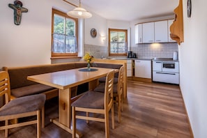 Une cuisine avec des meubles de rangement en bois, une table à manger avec des chaises, un vase rempli de fleurs et une croix accrochée au mur.