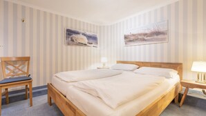 Habitación de hotel con cama doble, una silla de madera, dos cuadros en la pared y una mesita de noche con lámpara.
