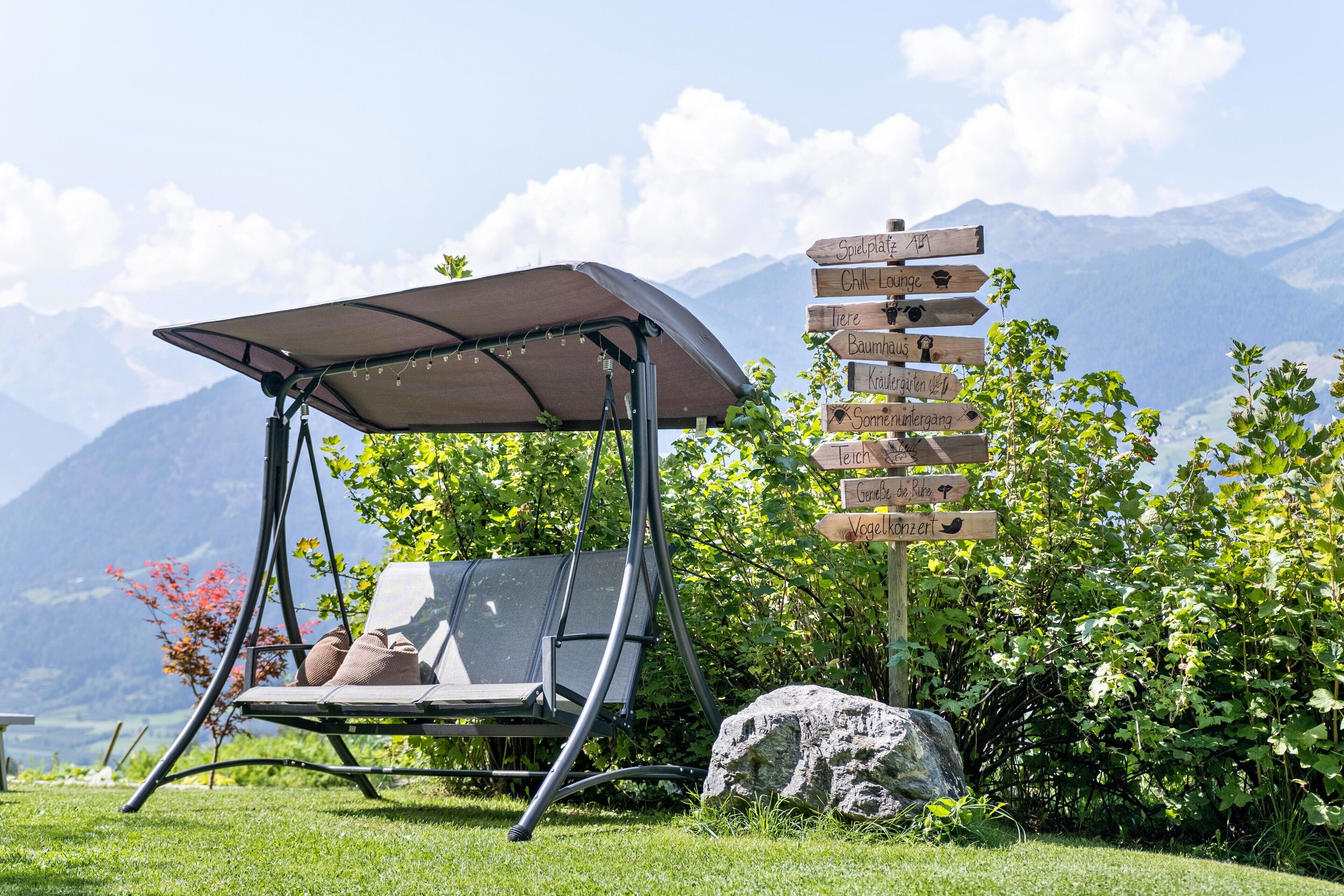 A garden with a swing chair, a rock, and a wooden signpost with various destinations.