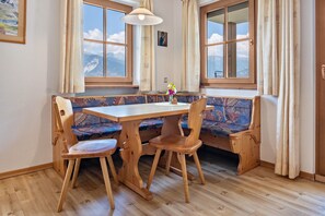 Une table de salle à manger en bois, avec des chaises, un banc et une fenêtre donnant sur les montagnes.