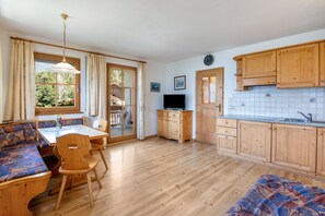 Une pièce comprenant une table à manger, des chaises, un banc, un téléviseur, des meubles en bois et une fenêtre avec des rideaux.