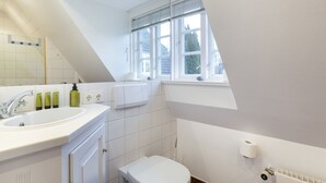 Moderni kylpyhuone, jossa on valkoinen pesuallas, peili ja wc-istuin. Huoneessa on ikkuna, jossa on sälekaihtimet, pyyhekoukku ja patteri.