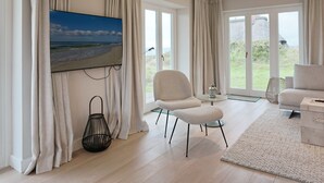 Amplia sala de estar con un televisor de pantalla plana grande, asientos cómodos y vistas al exterior a través de amplias ventanas.