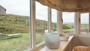Habitación con ventanas amplias que dan a un espacio verde y colinas. Hay un banco afuera de la ventana y un florero de vidrio en el alféizar.