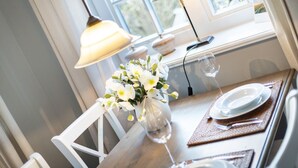 A dining table with a vase of white flowers, two table lamps, a wine glass, and a laptop on a windowsill. - Paulas Hüs - Fiete - Die Fiete, ca. 50 m² ist Besonders Liebevoll für bis zu 3 Personen (Sylt-Ost)