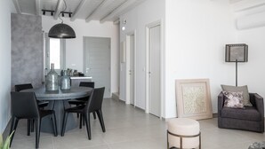 A modern dining area with a round table, black chairs, and a pendant light. There is a gray sofa with a cushion and a framed picture on the wall. - Petra Mare in Mykonos (Mykonos)