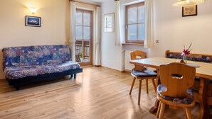 A room with a sofa, wooden dining table, chairs, and a window with curtains. - Apartment 'Patztauhof Tschavalatsch' with Mountain View, Shared Garden and Wi-Fi (Sluderno BZ)