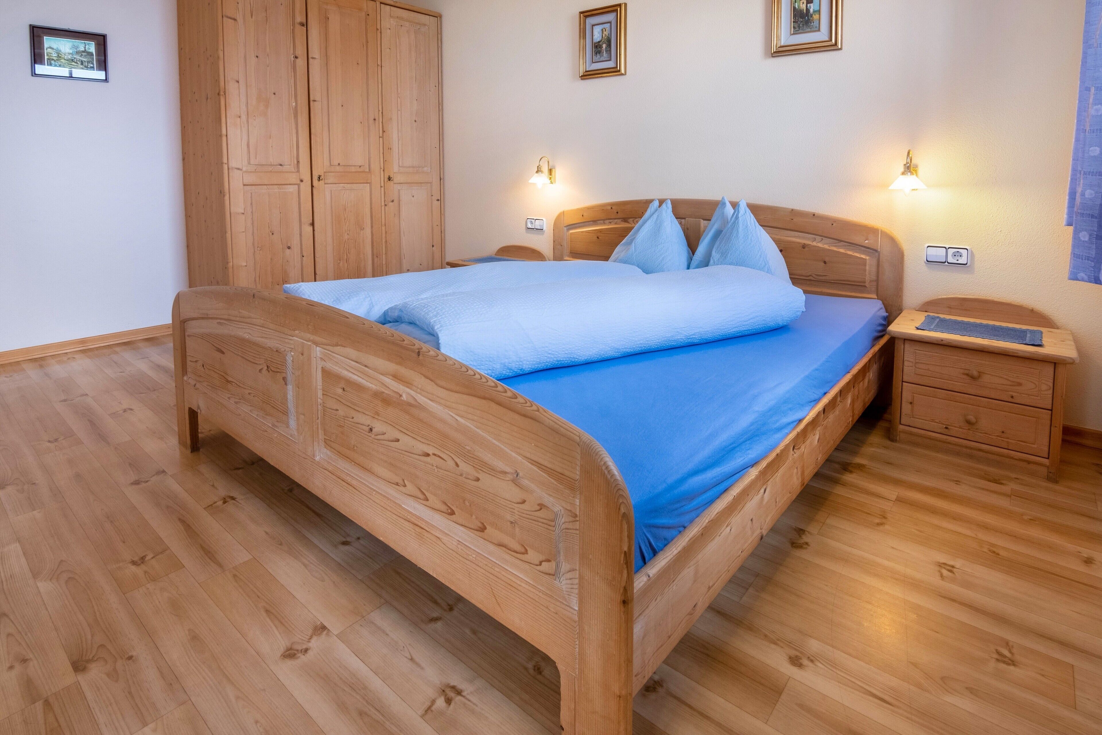 Un lit en bois avec un matelas et des oreillers bleus, une table de chevet avec une lampe et une armoire en bois.