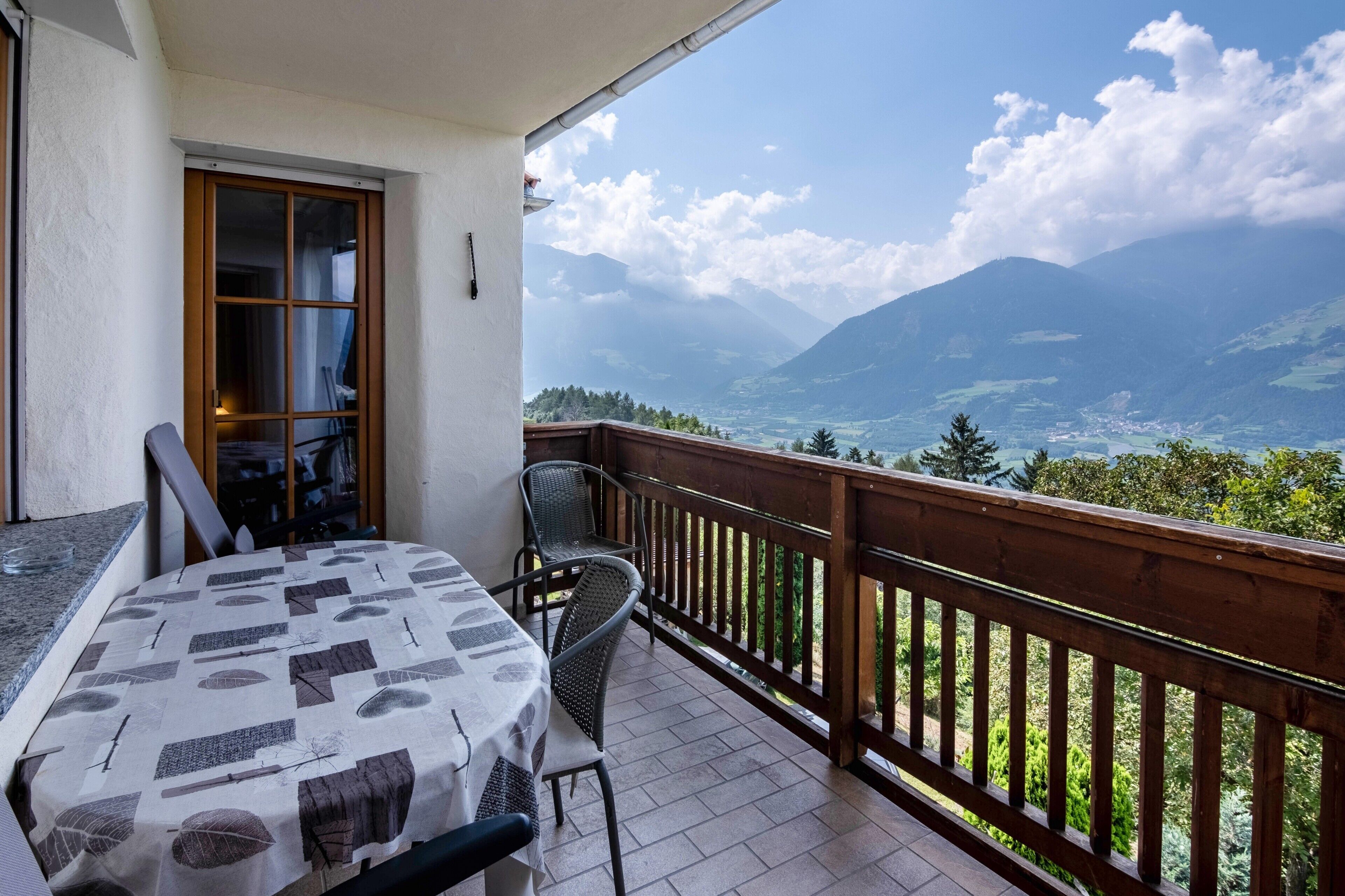 Un balcon avec une table et des chaises, une balustrade en bois et une vue sur les montagnes.