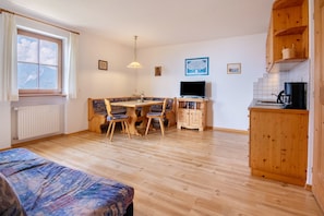 Une pièce comprenant un lit, une table à manger avec des chaises, un téléviseur, une machine à café et des armoires en bois.