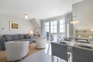 Uma sala de estar moderna com um sofá, uma mesa de jantar posta para dois e uma janela grande com cortinas.