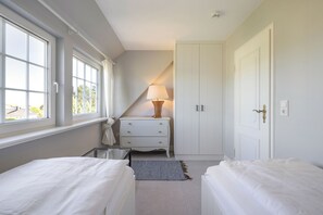 Quarto com duas camas, penteadeira, abajur e guarda-roupa.