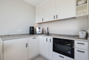 Uma cozinha moderna com armários brancos, forno embutido, cafeteira e dispenser de água.