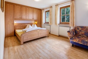 A bedroom with a wooden bed, a window with curtains, a radiator, and a sofa.