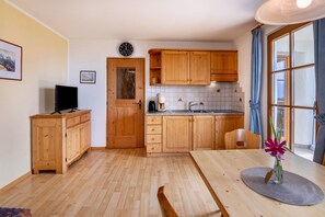 A kitchen with wooden cabinets, a sink, a clock, and a window with curtains.