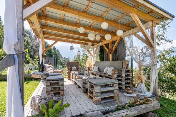 An outdoor wooden deck with rustic furniture, a covered seating area, and a view of the mountains.
