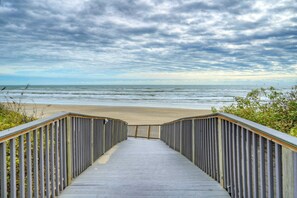 A wooden boardwalk leading to a beach with a cloudy sky.