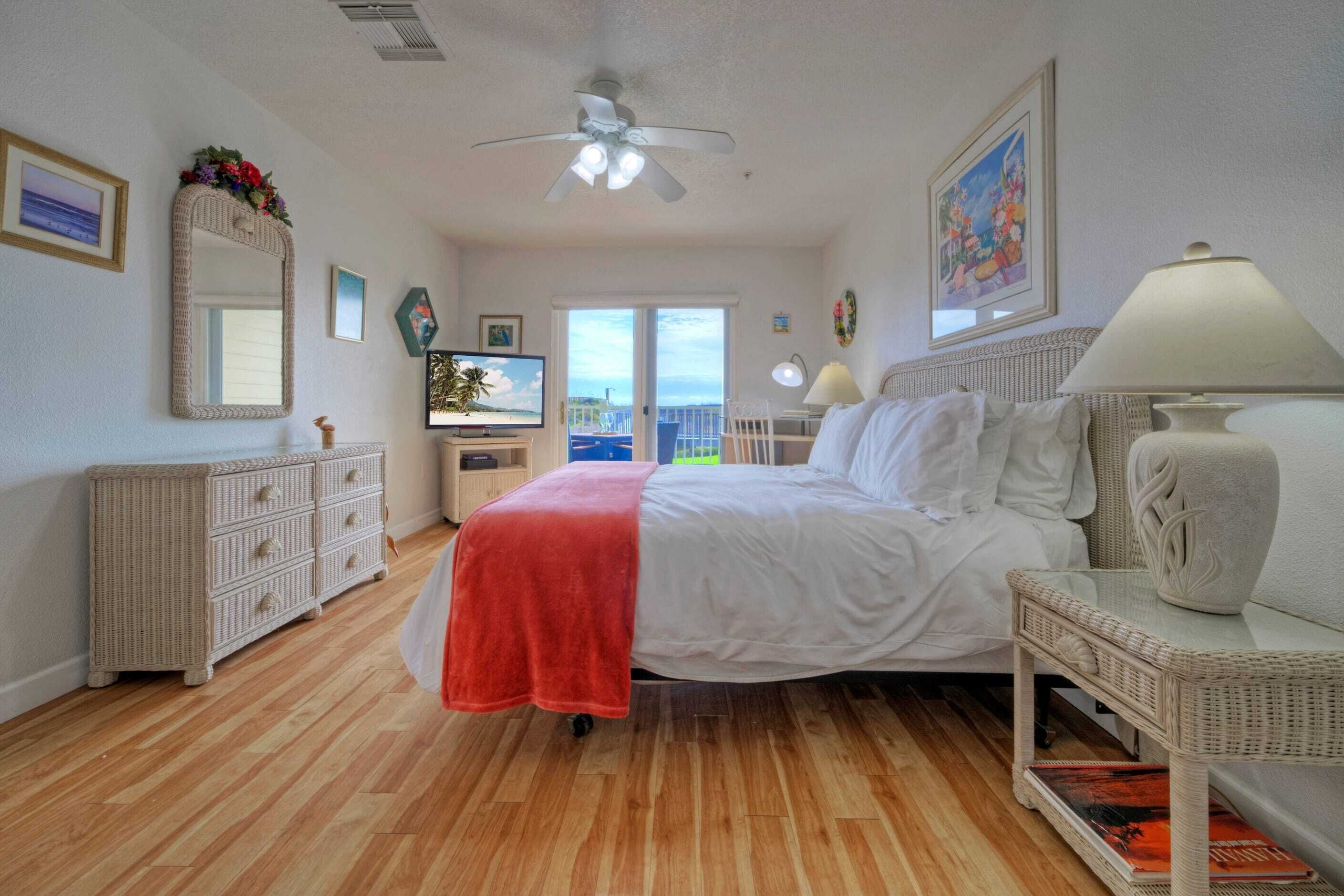 A bedroom with a bed, a dresser, a television, and a balcony with a view.