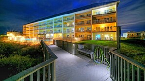A multi-story hotel with balconies, a pool area, and a well-lit deck. - Salt & Sun by Avantstay Beach Access + Pool (Port Aransas)