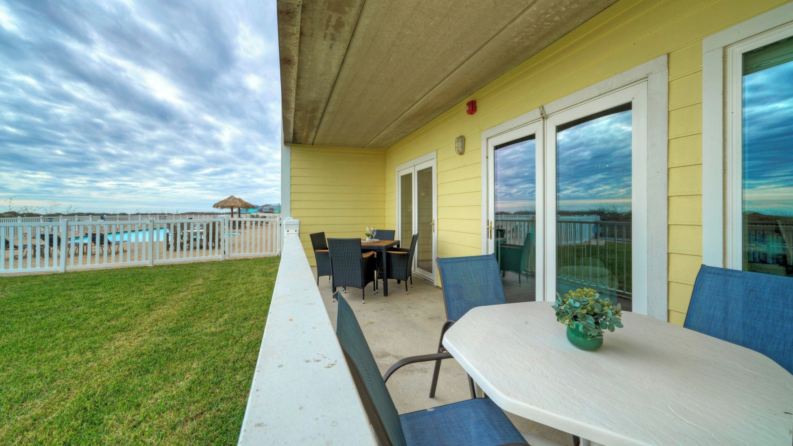 A patio with a table and chairs, a small plant, and a view of a pool and beach.