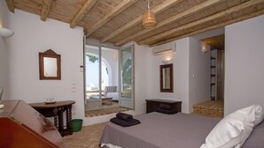 A bedroom with a wooden ceiling, a bed with a white pillow, a small table with a mirror, and a view of an outdoor area through a glass door. - Baroness in Mykonos With 5 Bedrooms and 4 5 Bathrooms (Mykonos)