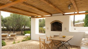 An outdoor patio with a brick floor, wooden furniture, and a stone wall with a brick fireplace. - Baroness in Mykonos With 5 Bedrooms and 4 5 Bathrooms (Mykonos)