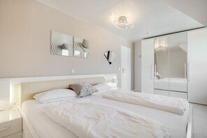 A modern bedroom with a large bed, bedside tables, a wardrobe, and wall-mounted mirrors.