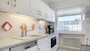 Une cuisine moderne avec des meubles blancs, un lave-vaisselle encastré, une machine à café et une fenêtre offrant une belle vue.