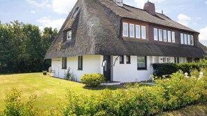 Une maison à toit de chaume, aux murs blancs, dotée d’un porche et d’un jardin bien entretenu.