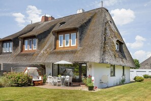 Une maison avec un toit de chaume, une terrasse avec des meubles d’extérieur et une façade blanche.