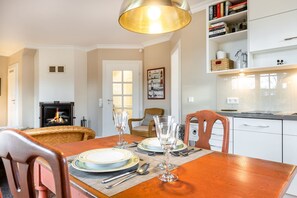A dining area with a wooden table set for two, a fireplace, and a kitchen in the background.