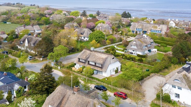 A coastal village with thatched-roof houses, a main road, and a view of the sea. - Elbe, Wohnung Nr. 8 - Haus Elbe - Liebevoll Ausgestattete Obergeschoss-wohnung Unter Reet (Sylt-Ost)