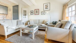 A modern living room with a sofa, a coffee table, and a bookshelf. - Elbe, Wohnung Nr. 8 - Haus Elbe - Liebevoll Ausgestattete Obergeschoss-wohnung Unter Reet (Sylt-Ost)