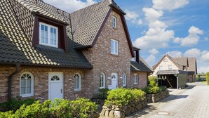 A traditional brick building with a steeply pitched roof, multiple windows, and a stone pathway leading to a gate.