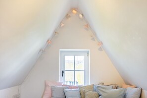 Una camera da letto mansardata accogliente, con un soffitto spiovente, un'ampia finestra e un letto con molti cuscini.