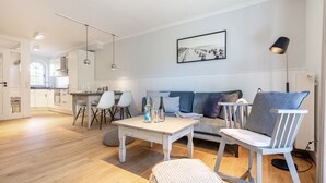 A modern living room with a sofa, chairs, a coffee table, and a dining area with a kitchen in the background.