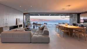 A modern living room with a large sofa, dining area, and a view of the sea. - Villa Sky II in Mykonos (Mykonos)
