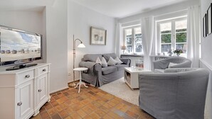A modern living room with a grey sofa, a white side table, and a flat-screen TV on a cabinet.