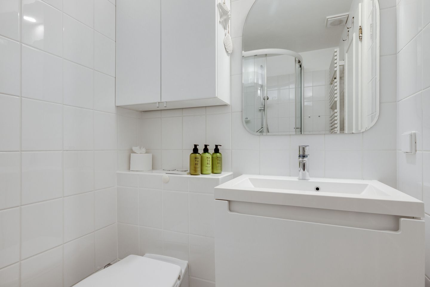 A modern bathroom with white tiles, a white sink, a mirror, and a shower enclosure.