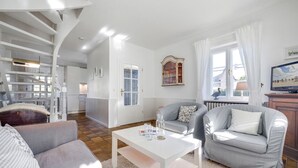 Ein geräumiges Wohnzimmer mit einem weißen Couchtisch, grauen Sofas und einer Treppe, die zu einer oberen Etage führt.