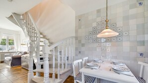 Ein Essbereich mit einem weißen Tisch, gedeckt für vier Personen, einer Treppe mit weißen Spindeln und einer gefliesten Wand mit kreisförmigen Mustern.