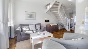 Ein geräumiges Wohnzimmer mit einem grauen Sofa, einem weißen Couchtisch und einer Treppe, die in eine obere Ebene führt.