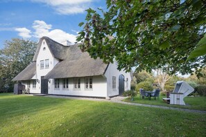 Ein weißes Haus mit Strohdach, einer Veranda und einem kleinen Garten mit Gartenmöbeln.