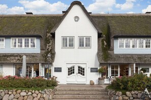 A traditional building with a steeply pitched roof, white exterior walls, and a central entrance with a double door.