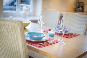 A dining table set with blue plates, silverware, and wine glasses, with a candle and a blue bowl on pink placemats.
