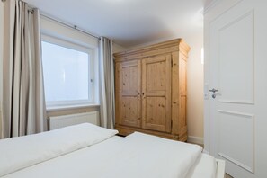 A bedroom with two beds, a wooden wardrobe, a window with curtains, and a door. - Barig Hüs EG - Barig Hüs EG - Objekt in Einer Ruhig Gelegenen Straße in der Nähe vom Wattenmeer (Sylt-Ost)