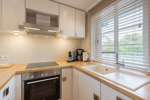 A modern kitchen with a built-in oven, a coffee maker, and a window with blinds.