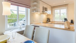 A modern kitchen with a dining area, featuring a large window, built-in cabinets, and a coffee machine.